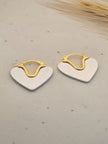 Pair of two-tone heart hoop earrings with gold-tone lever-back and brushed silver heart charm on speckled beige surface