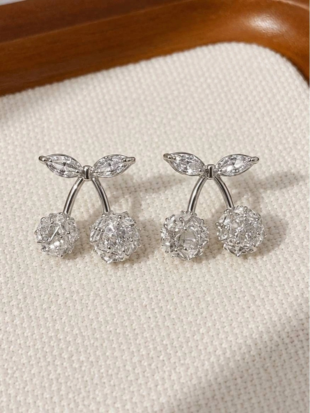 Pair of silver-finish cherry stud earrings with zirconia crystal spheres and marquise leaf accents on cream fabric