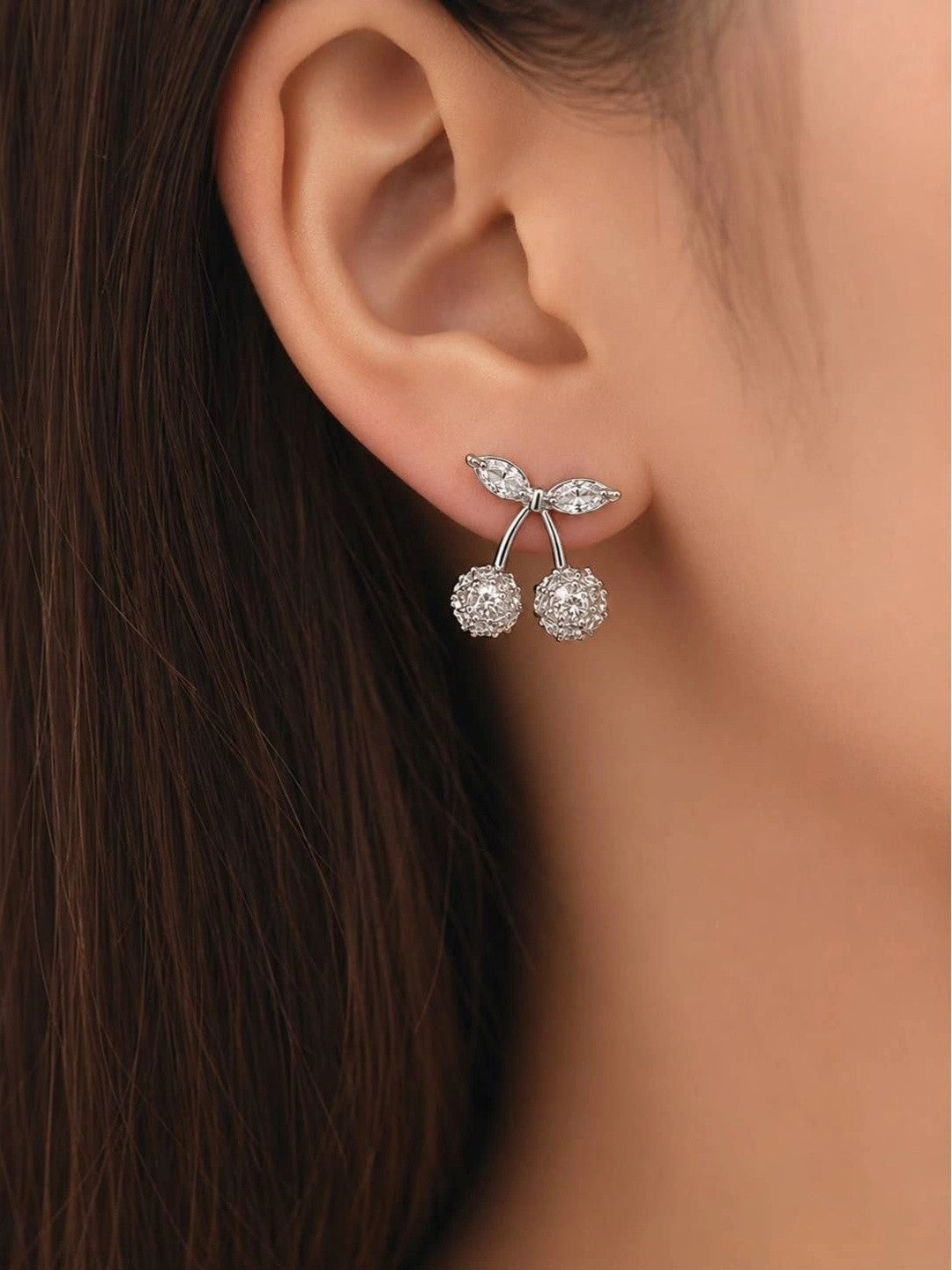 Silver zirconia cherry stud earring worn on a woman's ear showing scale and fit against dark hair