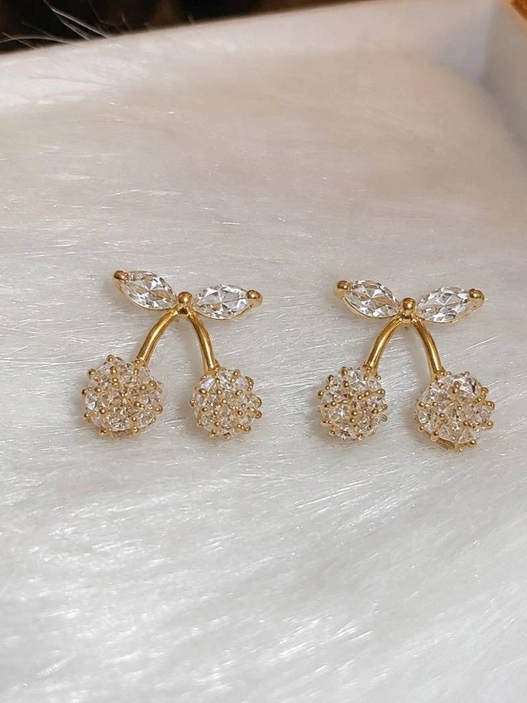 Two gold-plated cherry crystal stud earrings displayed on a white textured surface with close-up detail of cubic zirconia stones