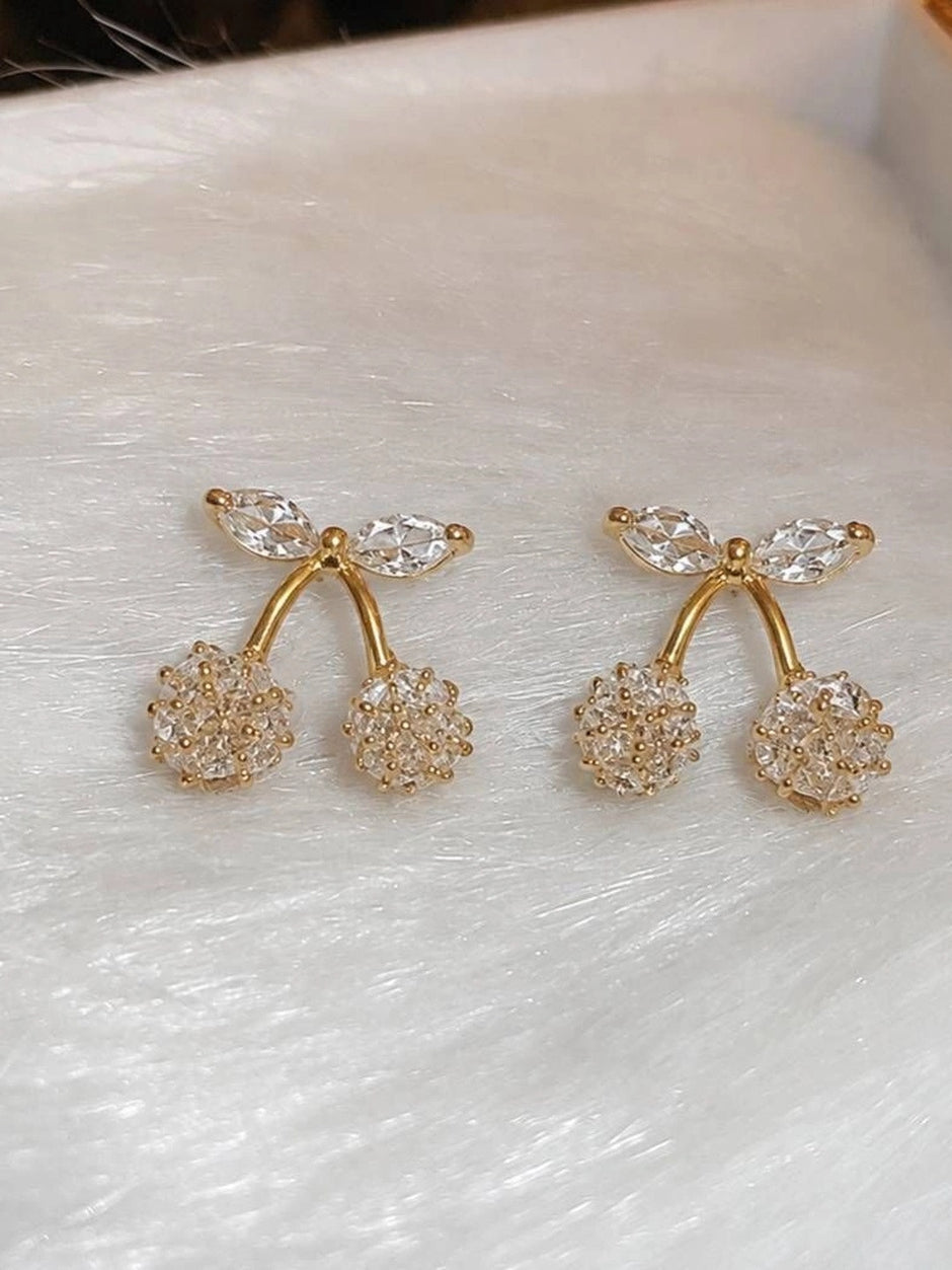 Two gold-plated cherry crystal stud earrings displayed on a white textured surface with close-up detail of cubic zirconia stones