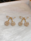 Two gold-plated cherry crystal stud earrings displayed on a white textured surface with close-up detail of cubic zirconia stones