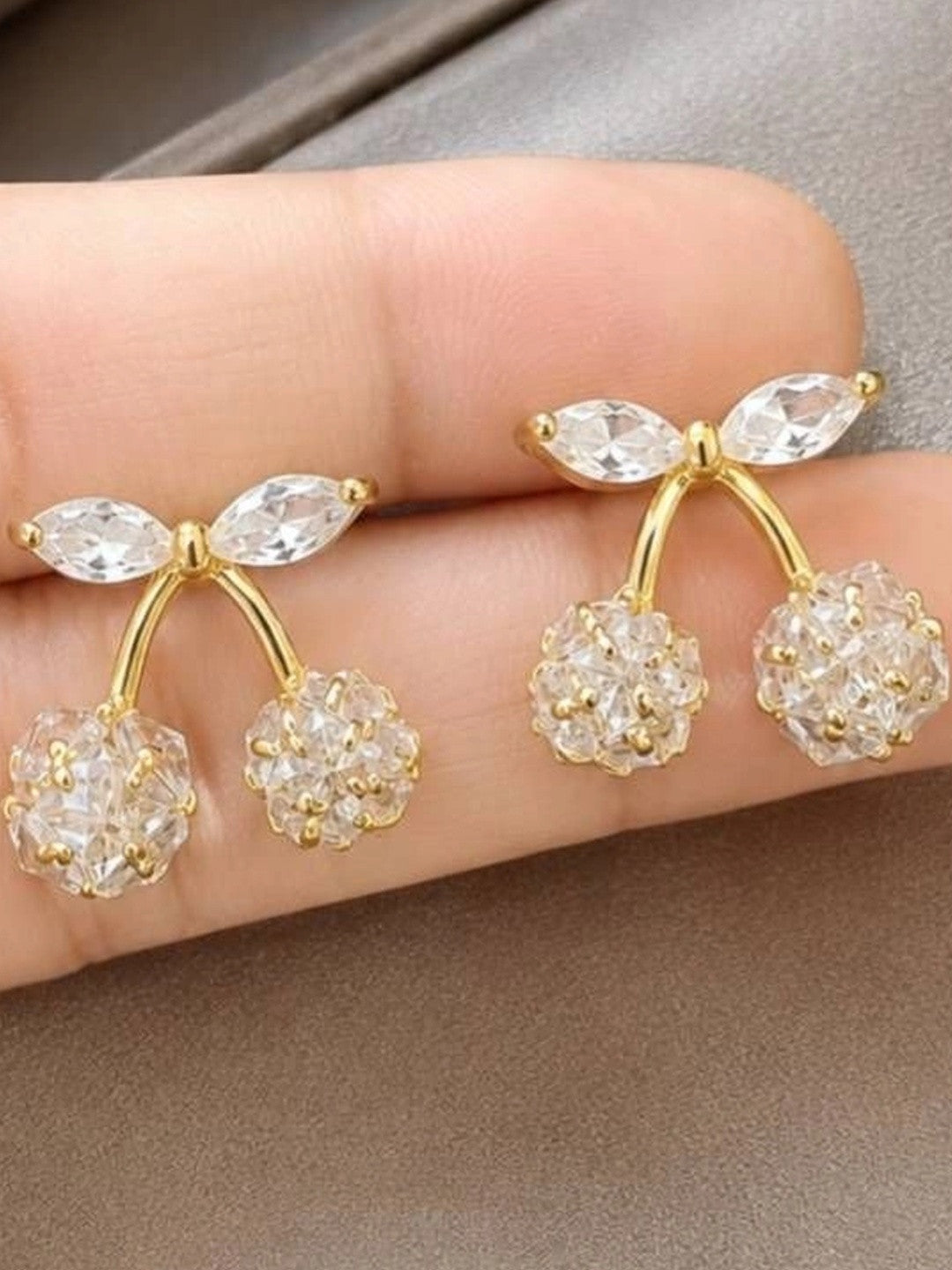 Both crystal cherry stud earrings resting on a person's fingertips showing scale and gold-tone finish in natural light
