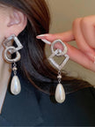 Silver geometric drop earring worn on ear, faux pearl teardrop visible alongside a matching earring held between fingers