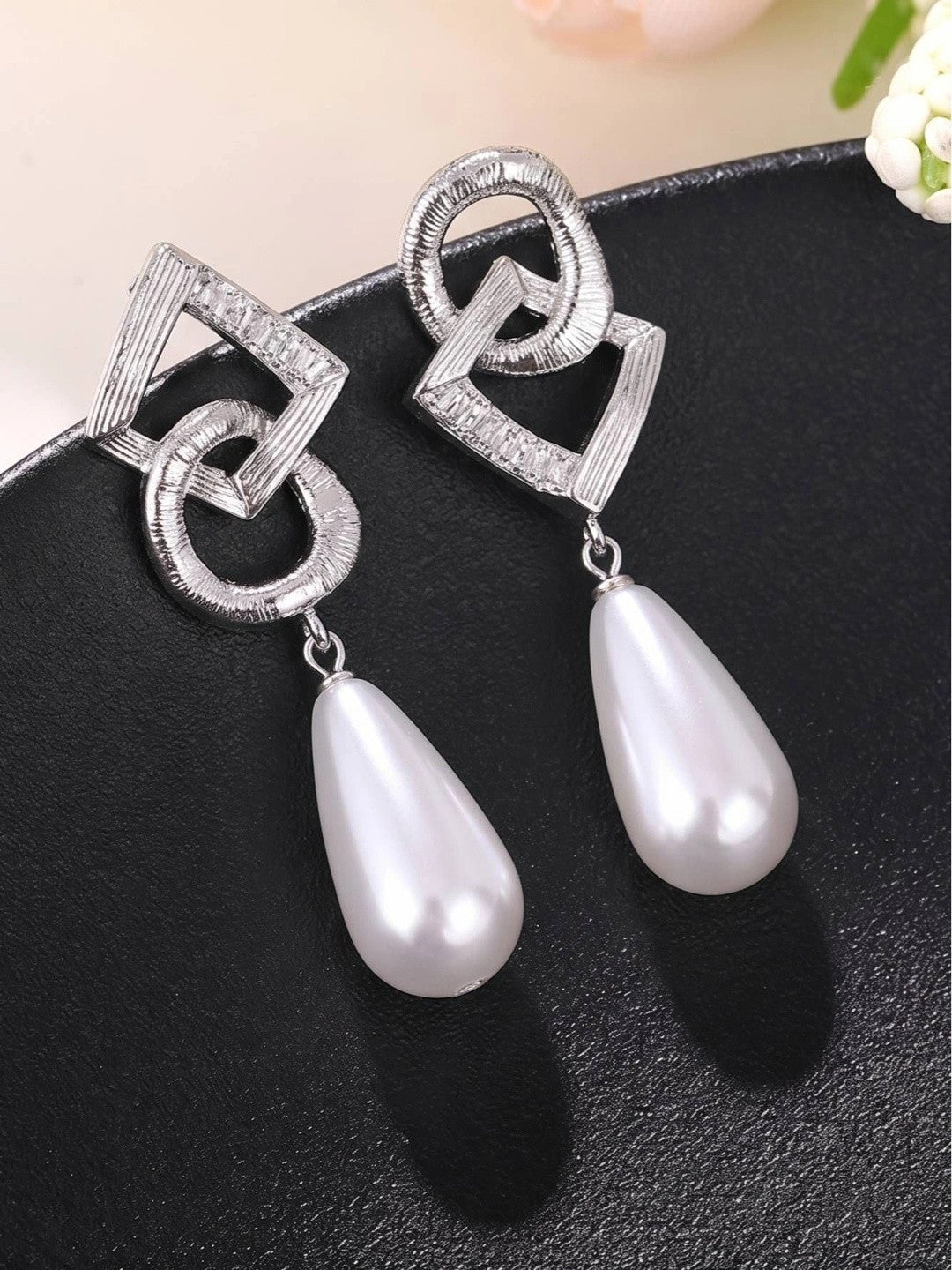Pair of silver interlocking circle and diamond geometric earrings with white faux pearl drops on black surface
