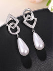 Pair of silver interlocking circle and diamond geometric earrings with white faux pearl drops on black surface