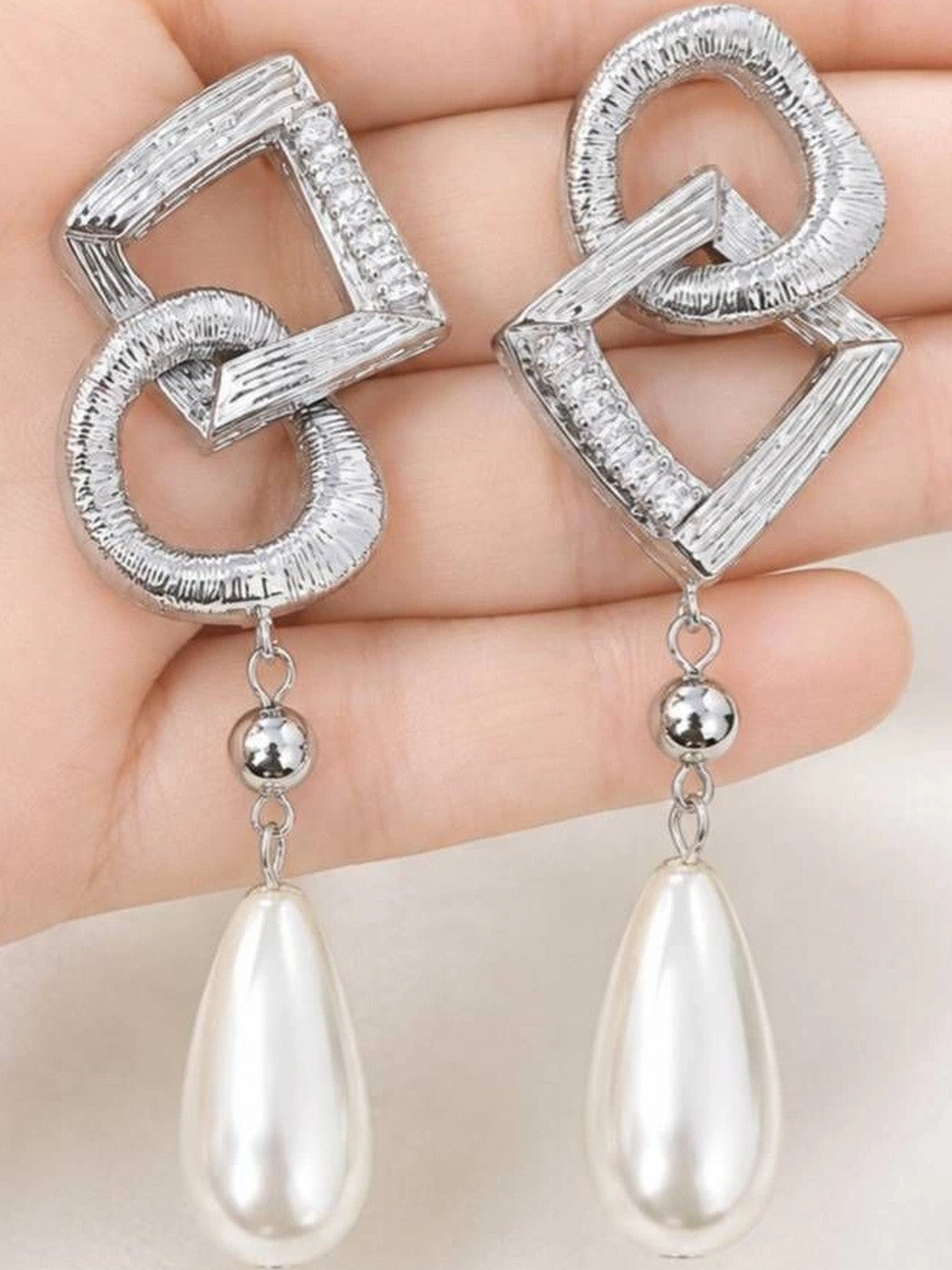 Both silver geometric pearl drop earrings displayed on a flat palm showing full front design detail