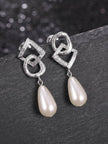 Silver geometric pearl drop earrings laid on dark slate surface with bokeh sparkle background