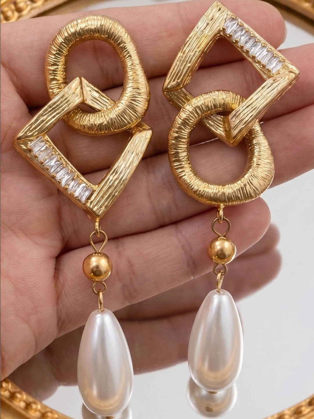 Both geometric gold earrings with large faux pearl drops held flat on an open palm