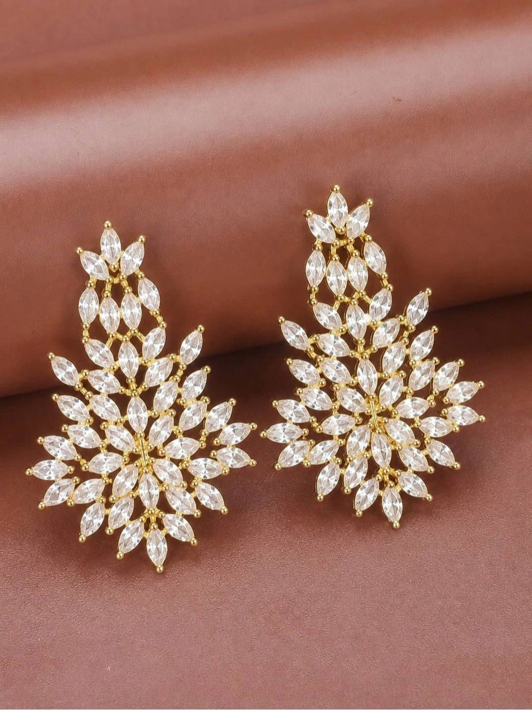 Pair of gold-plated marquise cubic zirconia floral drop earrings laid flat on a mauve surface