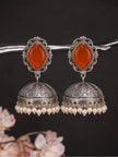 Pair of oxidised silver jhumka earrings with orange carnelian stone tops and ivory pearl fringe, displayed on a dark branch