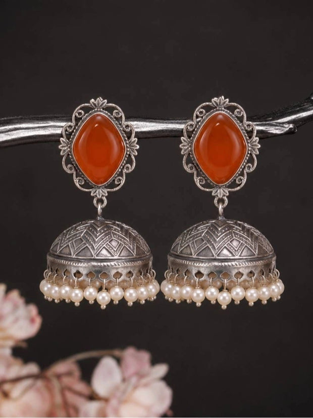 Pair of oxidised silver jhumka earrings with orange carnelian stone tops and ivory pearl fringe, displayed on a dark branch