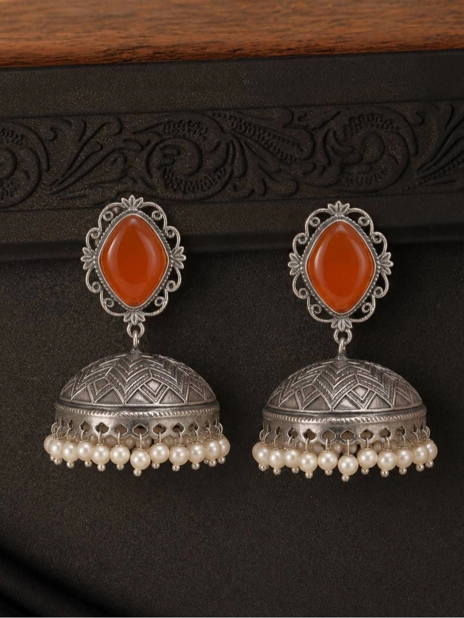 Front-facing flat lay of oxidised silver jhumka earrings with carnelian tops and geometric dome, against dark textured background