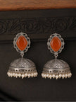 Front-facing flat lay of oxidised silver jhumka earrings with carnelian tops and geometric dome, against dark textured background