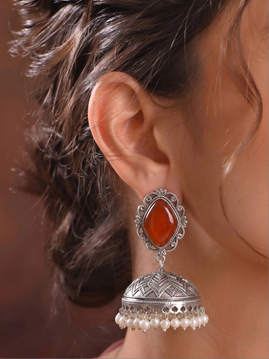 Close-up side profile of oxidised silver carnelian jhumka earring worn on a model's ear, showing pearl bead drop