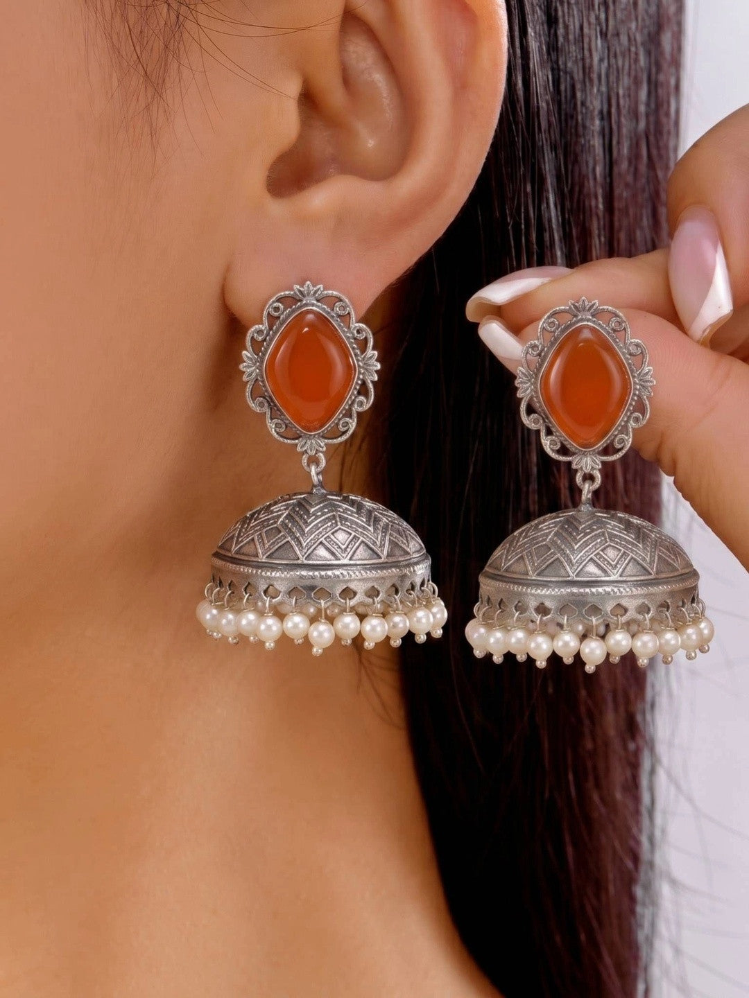 Model holding oxidised silver jhumka earring pair near her ear, showing scale and pearl fringe detail clearly