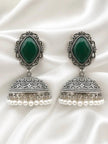 Both oxidised silver green stone jhumka earrings laid flat on white satin fabric showing engraved floral dome detail