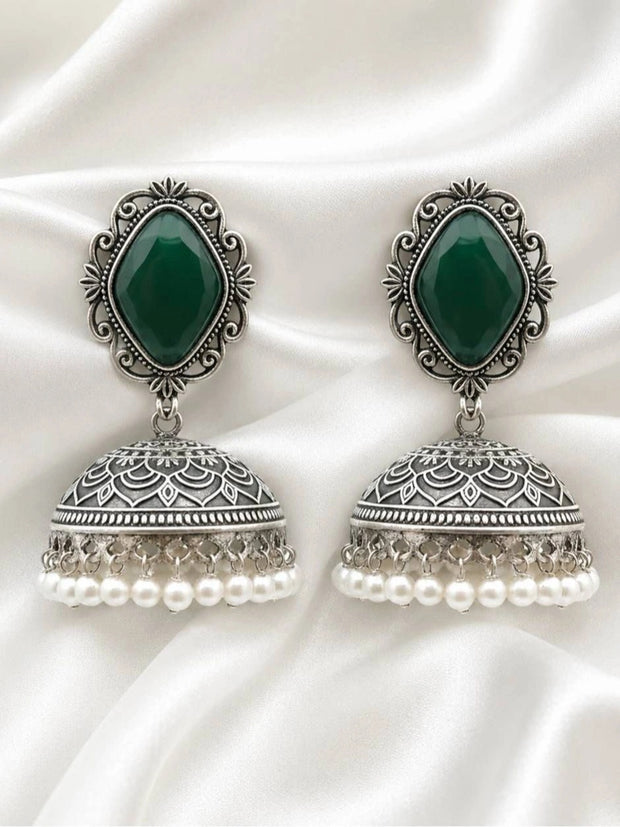 Both oxidised silver green stone jhumka earrings laid flat on white satin fabric showing engraved floral dome detail