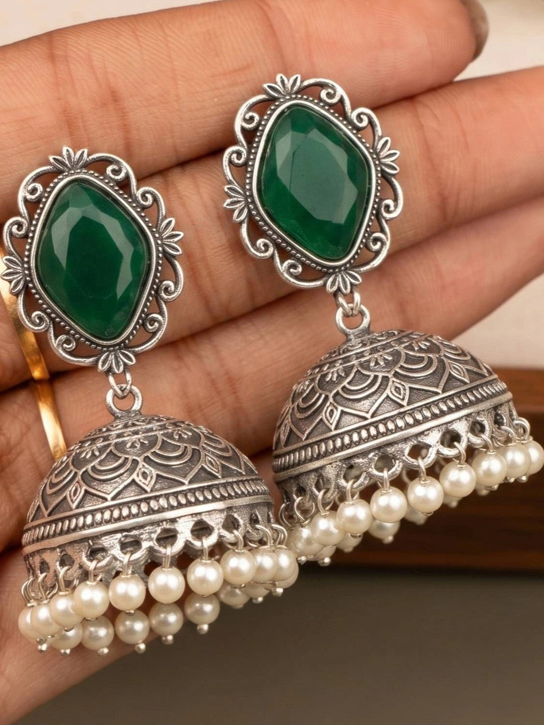Pair of oxidised silver jhumka earrings with pearl drops resting on an open palm showing intricate mandala engraving