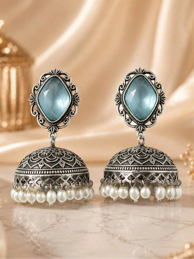 Pair of oxidised silver jhumka earrings with blue stone top and white pearl drops on marble surface