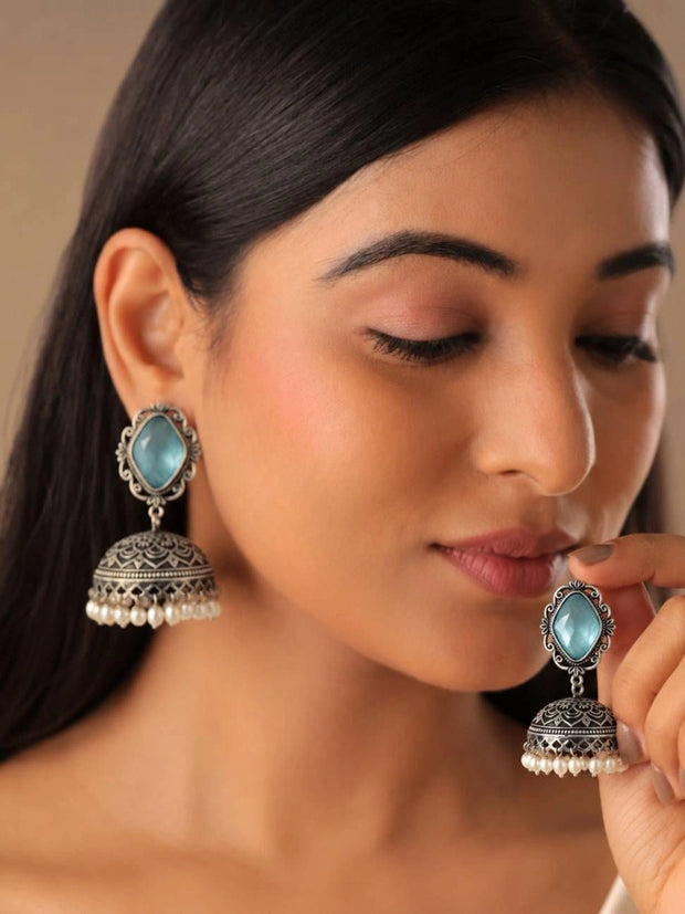Model wearing oxidised silver blue stone jhumka earrings, hand raised near face showing both ears