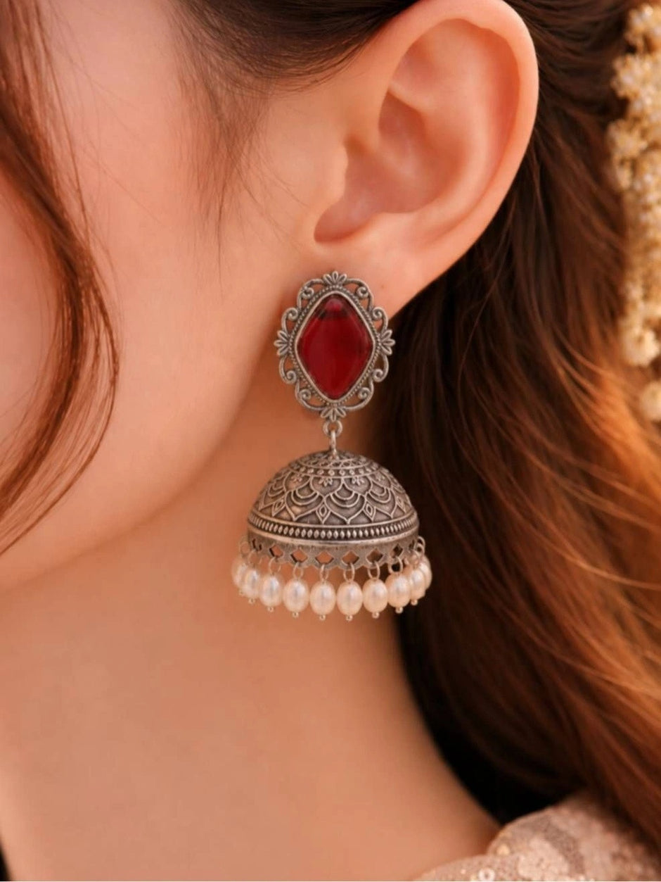 Oxidised silver jhumka earring with red stone stud worn on a woman's ear against soft neutral background