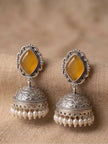 Pair of oxidised silver jhumka earrings with yellow diamond-shaped stones and pearl drop fringe, placed on beige fabric