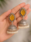 Close-up of two oxidised silver jhumka earrings with yellow stones and pearl drops resting on an open palm