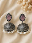 Pair of oxidised silver jhumka earrings with lilac stone tops and white pearl drops on cream fabric