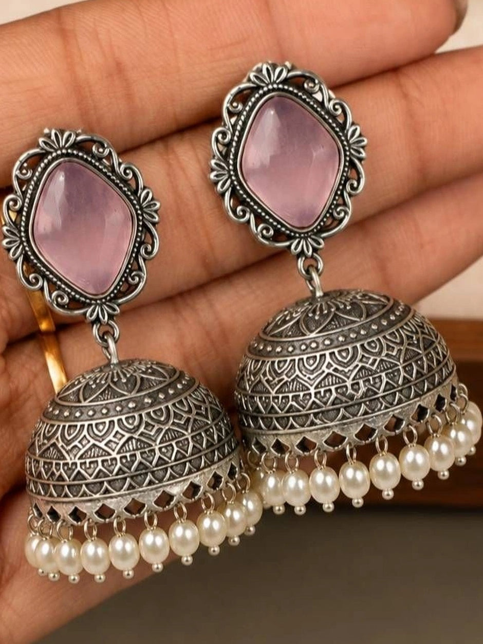 Two oxidised silver jhumka earrings with lilac stone frames and pearl drops resting on a palm