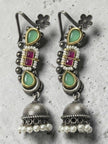 Oxidised silver jhumka earrings with ruby-red kundan centre and mint stones on a grey concrete background