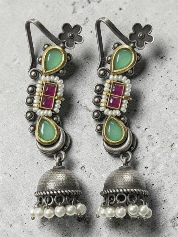 Oxidised silver jhumka earrings with ruby-red kundan centre and mint stones on a grey concrete background
