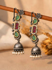 Pair of oxidised silver ear cuff jhumkas with green teardrop stones and pearl-trimmed red stone centre, hanging on a wooden rod