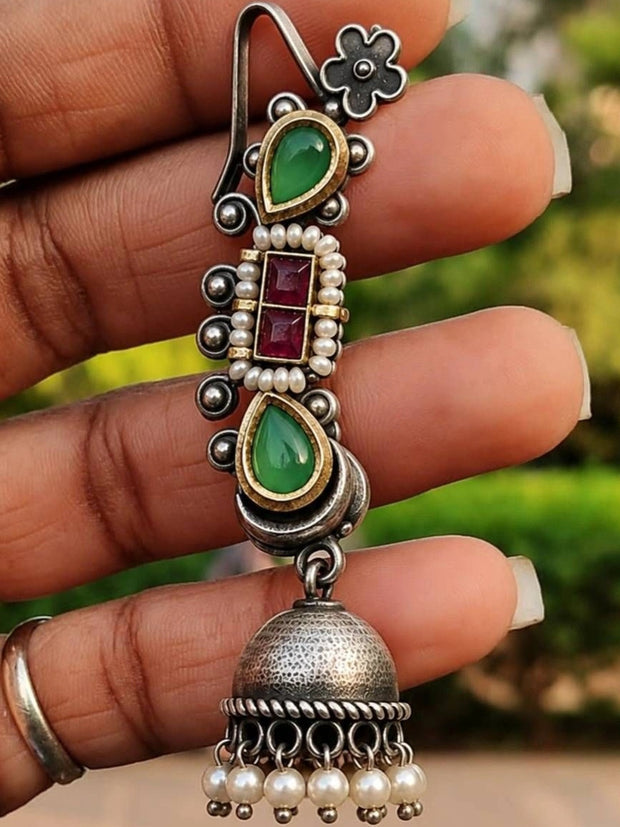 Single oxidised silver ear cuff jhumka held in a hand, showing green stones, pearl border, and dome bell with pearl drops