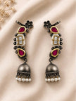 Pair of oxidised silver Kundan ear cuff jhumkas with ruby teardrops and pearl drops laid flat on ivory fabric