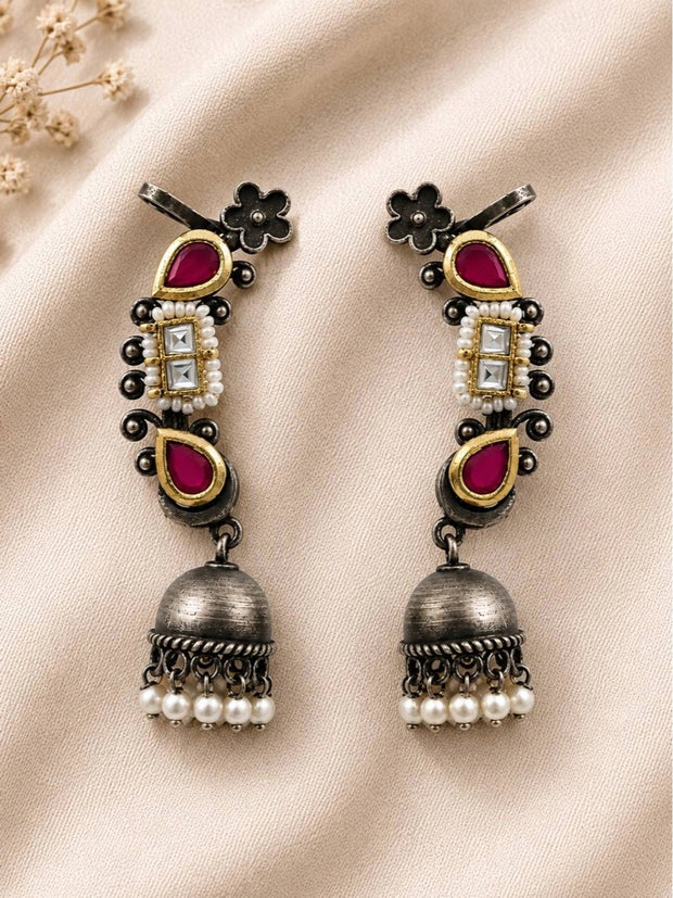 Pair of oxidised silver Kundan ear cuff jhumkas with ruby teardrops and pearl drops laid flat on ivory fabric