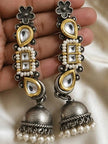 Two oxidised dual-tone kundan ear cuff jhumka earrings held in hand against ivory silk fabric