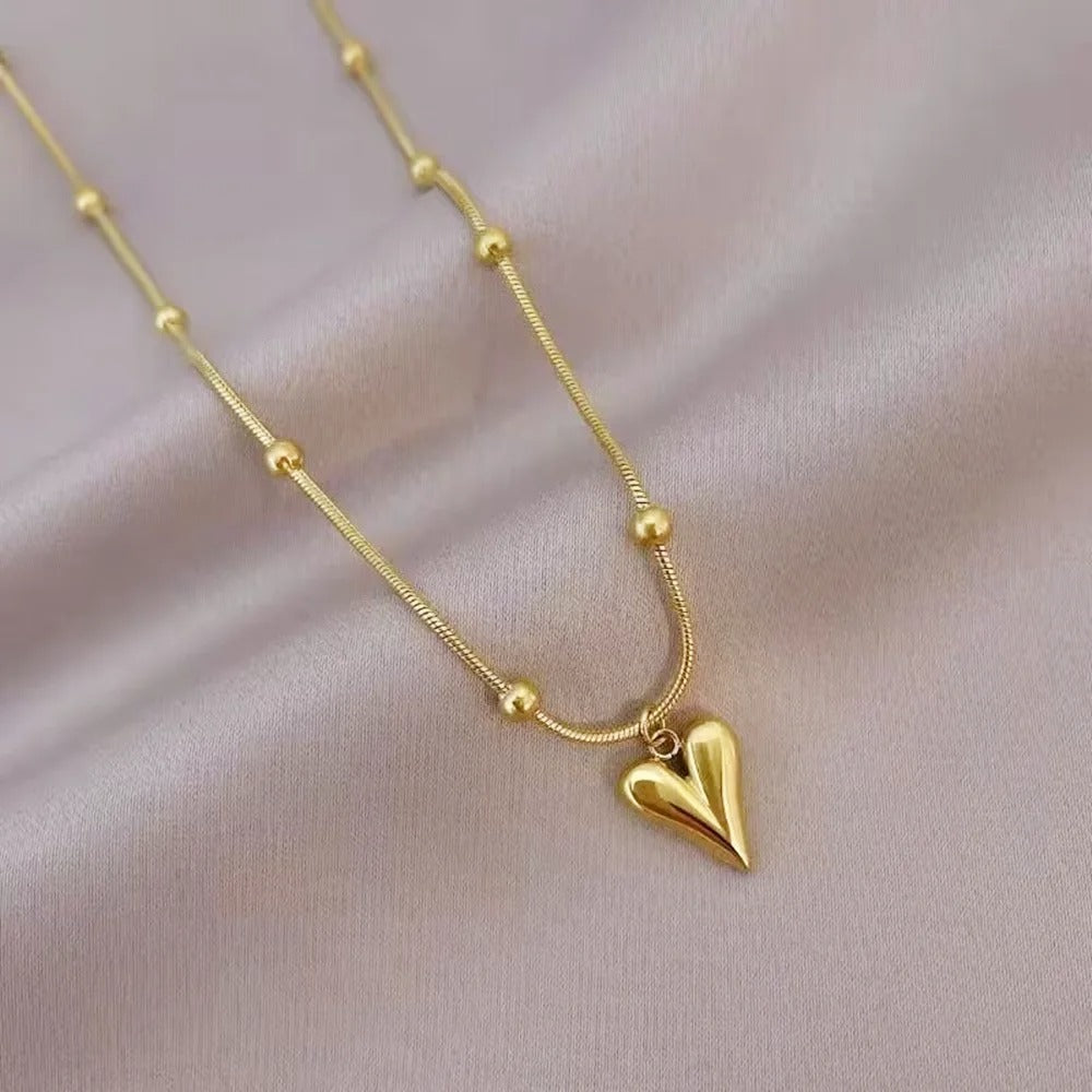 Elegant gold necklace with heart pendant and bead accents displayed on soft fabric.