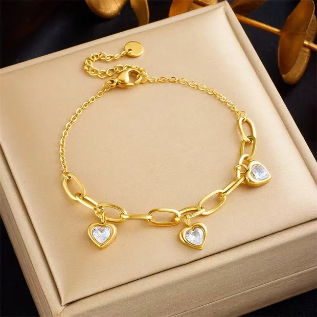 A gold-colored charm bracelet with heart-shaped pendants, presented in a box.