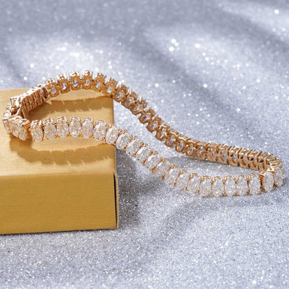 Rose gold tennis bracelet with oval-cut sparkling stones displayed on a golden box with a glittery background.