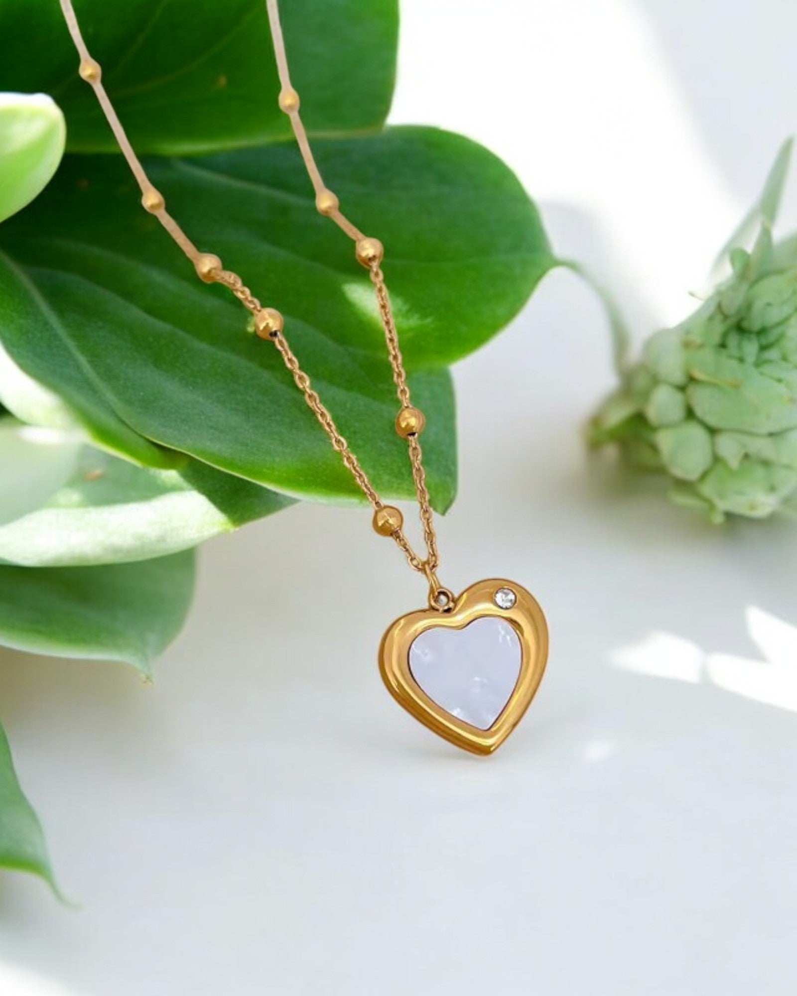 Gold heart pendant necklace with white enamel center and small diamond accent, elegant modern jewelry.