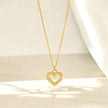 A gold heart-shaped pendant necklace with a hollow center, placed against a soft, draped background.