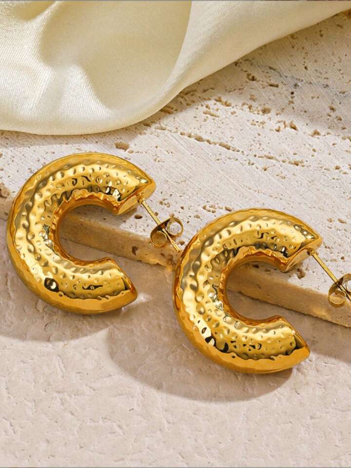 Gold hoop earrings on a textured beige surface