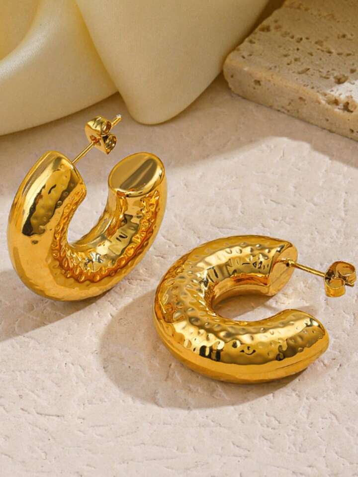 Gold hoop earrings on a textured beige surface