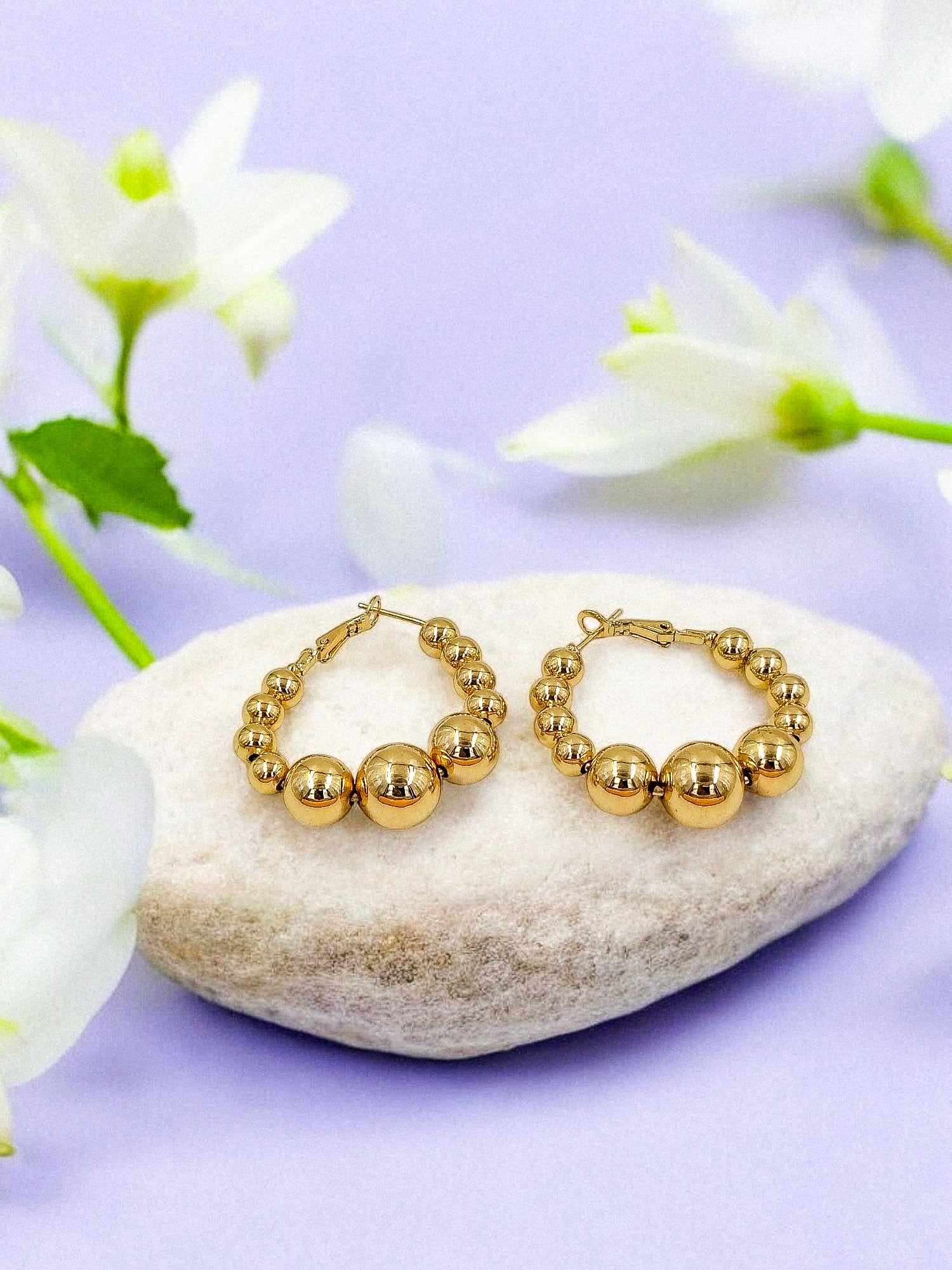 A pair of gold-colored beaded hoop earrings displayed against a floral background.