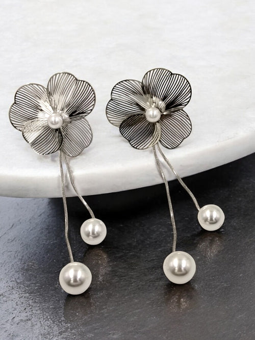 A pair of silver petal-shaped earrings with pearl drop designs, displayed on a marble surface.