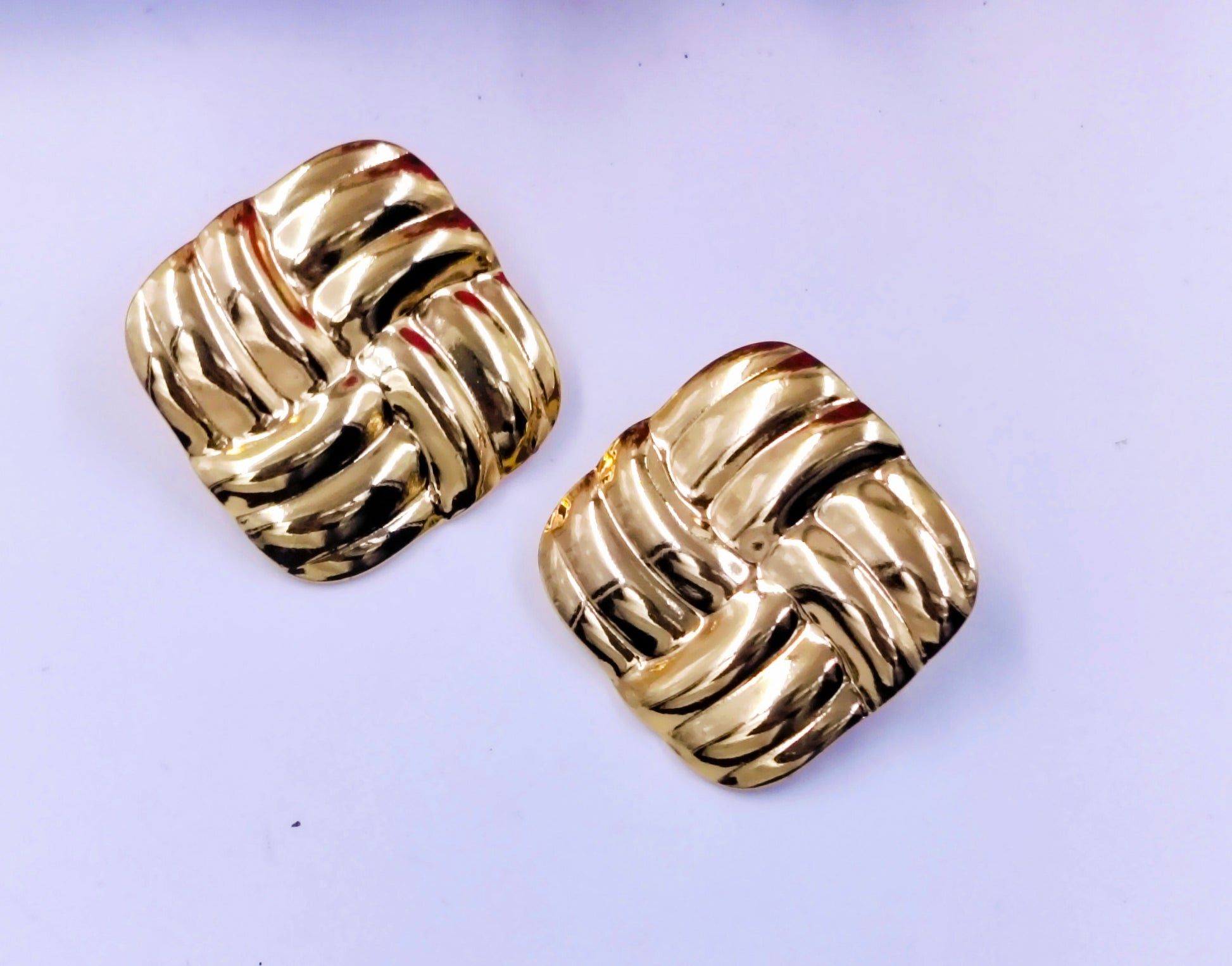 Glossy gold square stud earrings with a bold woven texture design, displayed on a plain white background.