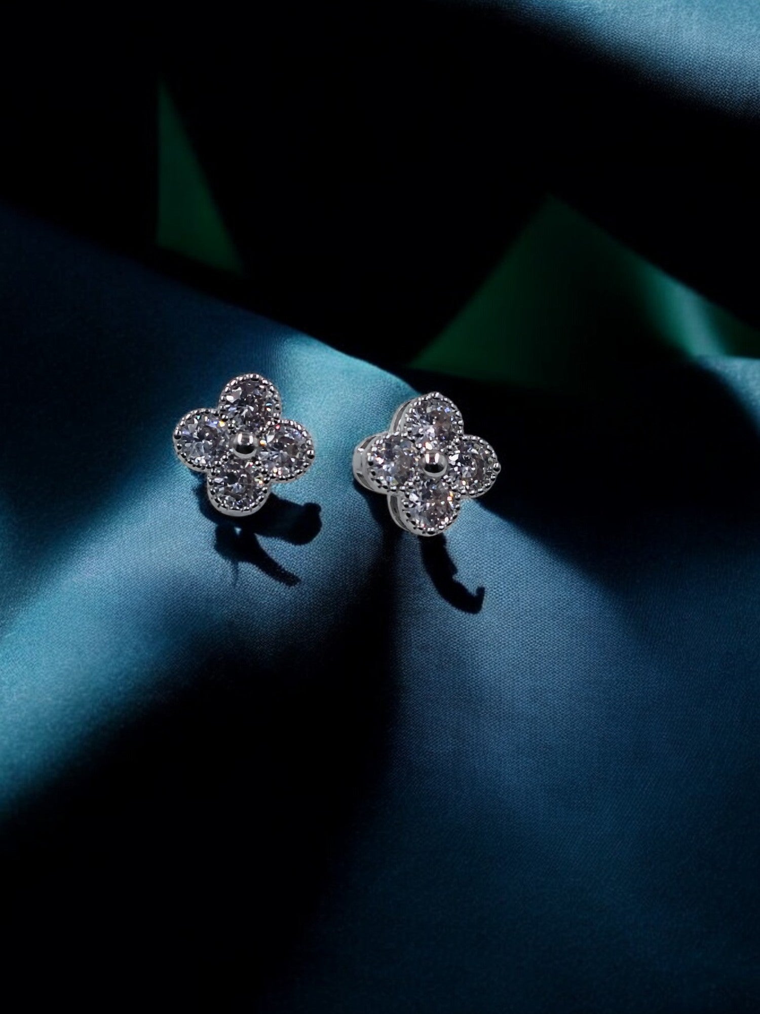 Stylish silver floral stud earrings with sparkling stones, elegant shine on dark fabric background, timeless beauty.