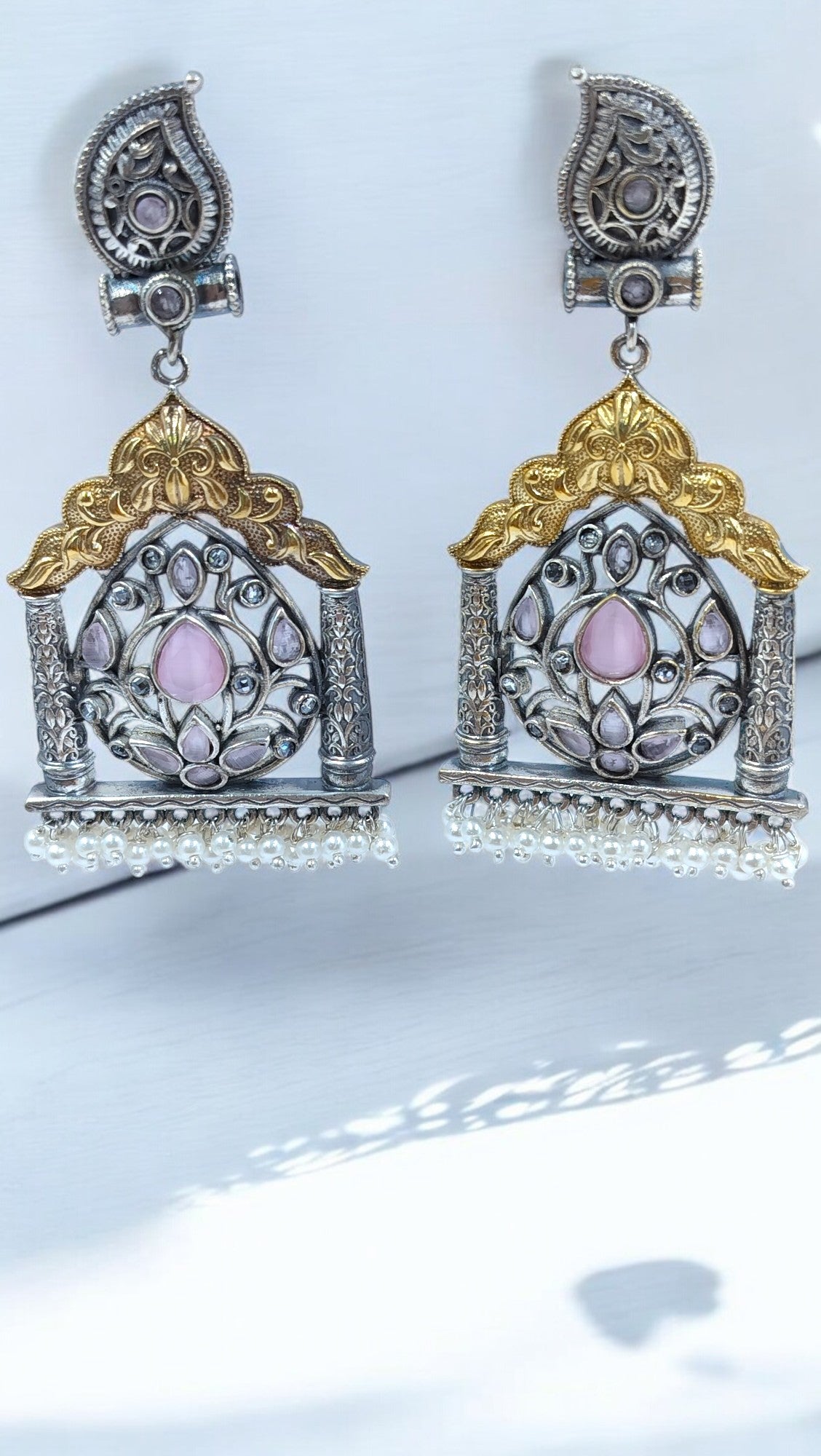 Elegant temple-style earrings in oxidised silver with golden arch, pink stone centerpiece, floral design and pearl drops.