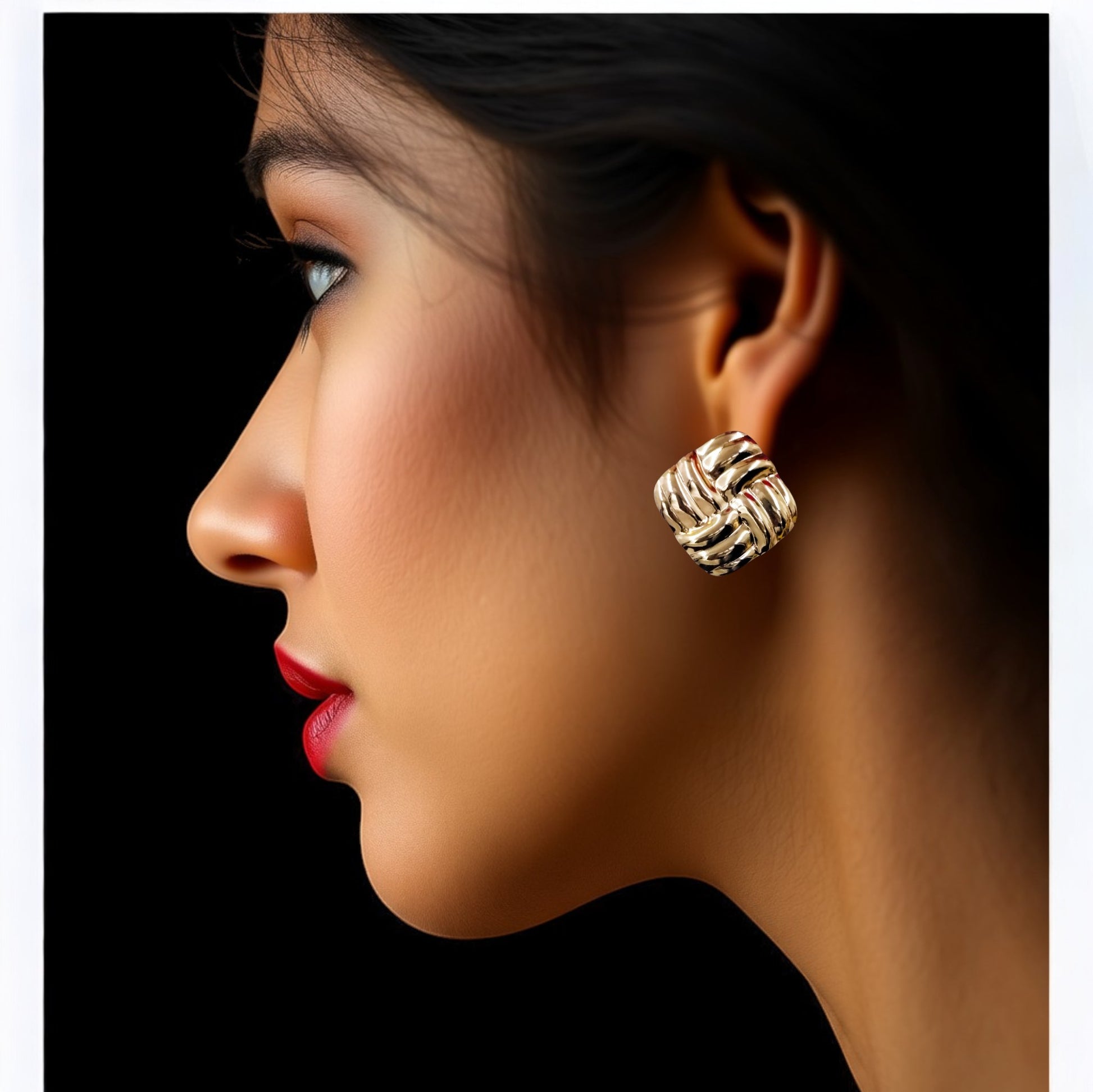 Side profile of a woman wearing bold gold square stud earrings with a woven textured design, set against a black background.
